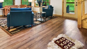 A spacious living room with wooden floors, a high ceiling, and large windows offering views of greenery. - Smokies Private Pool Cabin, Sleeps 14,Theatre & Game Room, Minutes from Parkway! (Sevierville)