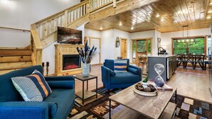 A spacious living area with a high ceiling, wooden staircase, and a fireplace.