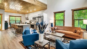 A spacious living area with a blue sofa, a coffee table, and a kitchen in the background. - Smokies Private Pool Cabin, Sleeps 14,Theatre & Game Room, Minutes from Parkway! (Sevierville)