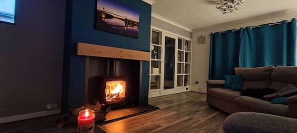 A cozy living room with a wood-burning stove, a sofa, and a large window with curtains.