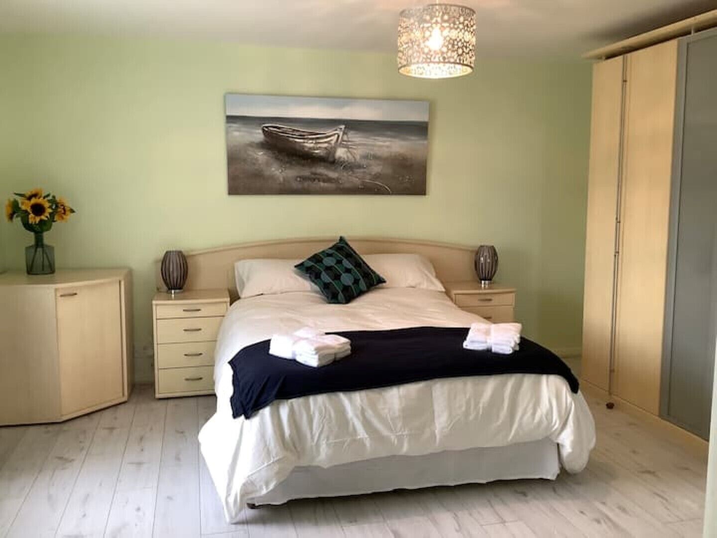 Una camera da letto con un letto, un comodino, una cassettiera, un quadro raffigurante una barca sull'acqua e un lampadario.