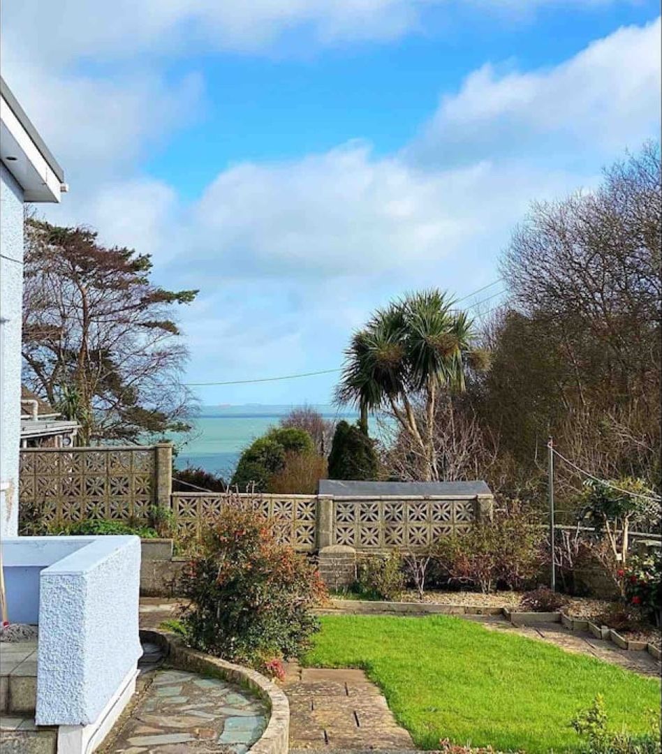 A garden with a lawn, a stone pathway, and a view of the sea.
