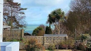 A garden with a lawn, a stone pathway, and a view of the sea. - Benllech Sea View bungalow, Dog Friendly sleeps 6 (Benllech)