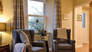 A room with two plaid armchairs, a small table with a vase of flowers, and a window with curtains. - A real gem of a cottage. (Alyth, near Blairgowrie)