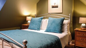 A bedroom with a bed, two nightstands, a lamp, a framed picture on the wall, and a wooden dresser. - A real gem of a cottage. (Alyth, near Blairgowrie)