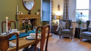 A dining area with a wooden table set for four, a fireplace, and two armchairs. - A real gem of a cottage. (Alyth, near Blairgowrie)
