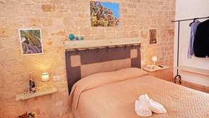 Een slaapkamer met een stenen muur, een bed met een beige sprei, een nachtkastje met een lamp en een afbeelding van een boom.