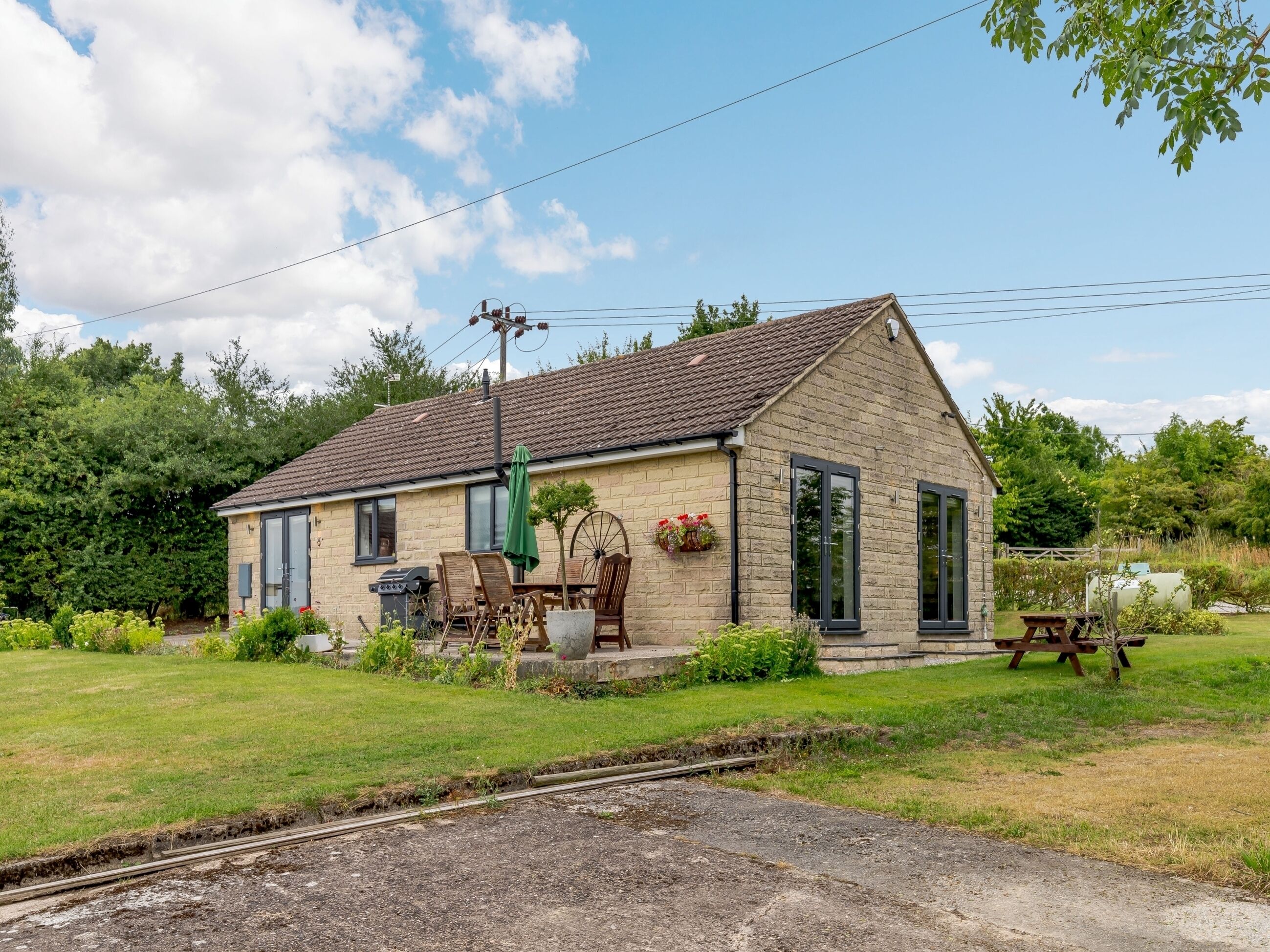 A small brick house with a tiled roof, a patio with outdoor furniture, and a garden.