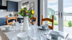 Un coin repas avec une table dressée pour quatre personnes, un vase de fleurs et une vue sur l’extérieur.