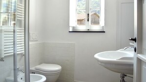 A bathroom with a toilet, a sink, and a window with a view of a house. - Medieval house in the countryside; 20 km from Alassio' beach (Vesallo)