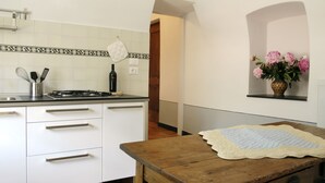 A kitchen with white cabinets, a wooden table, and a vase of flowers on the wall. - Medieval house in the countryside; 20 km from Alassio' beach (Vesallo)