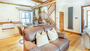 A spacious living area with a brown leather sofa, wooden staircase, and a dining table set for six. - 3 bedroom accommodation in Ingleton (Ingleton)