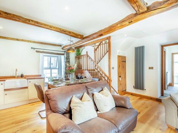 A spacious living area with a brown leather sofa, wooden staircase, and a dining table set for six. - 3 bedroom accommodation in Ingleton (Ingleton)