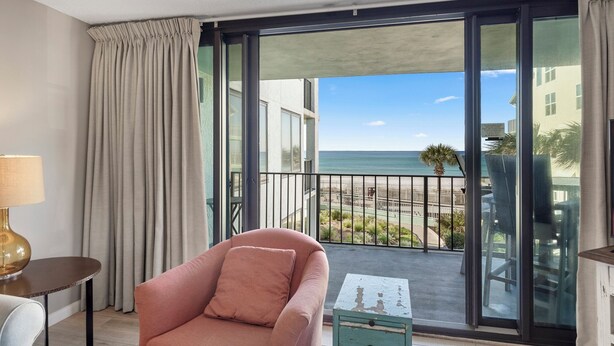 Un balcón con vista a la playa y al océano, una silla rosa y una lámpara.