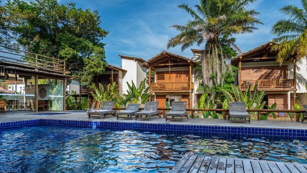 Zona de piscina con sillones, terraza de madera y vistas a los edificios del complejo.