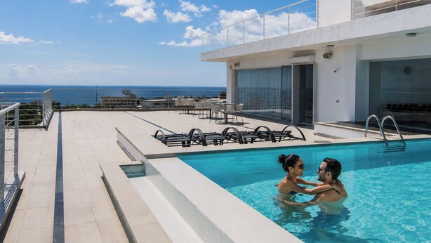 Una piscina en la azotea con vista al océano, puerta de entrada de vidrio y mobiliario exterior.