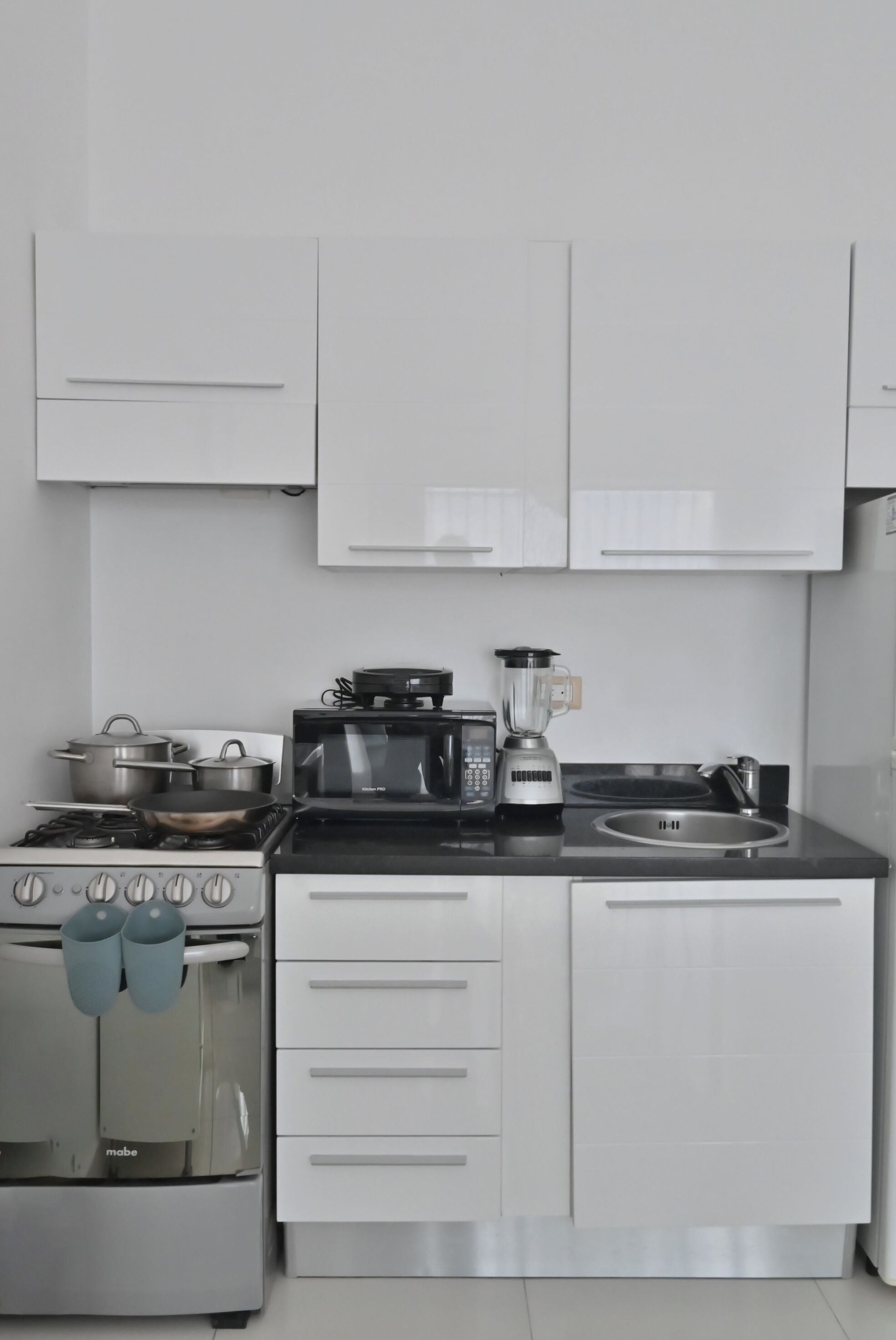 Een moderne keuken met witte kastjes, een fornuis, een magnetron en een spoelbak.