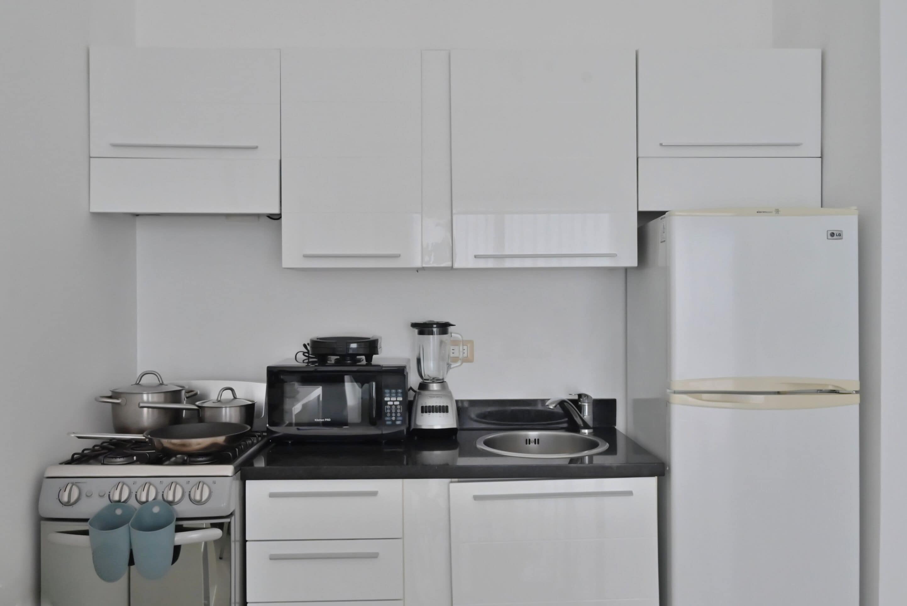 A kitchen with white cabinets, a stove, a microwave, a blender, and a refrigerator.