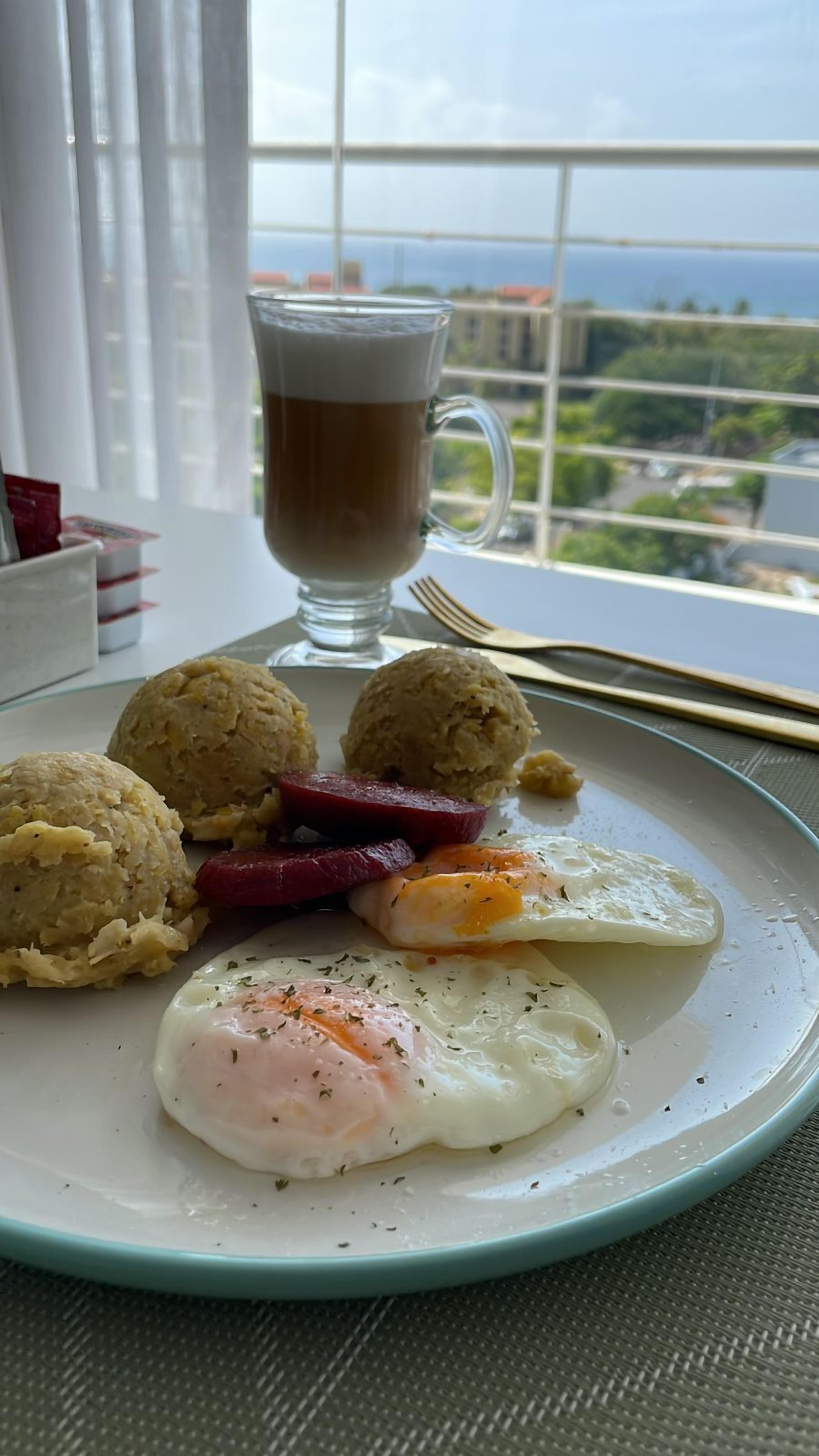 En tallerken med æg, pølse og småkager, samt et glas kaffe på et bord ved et vindue.