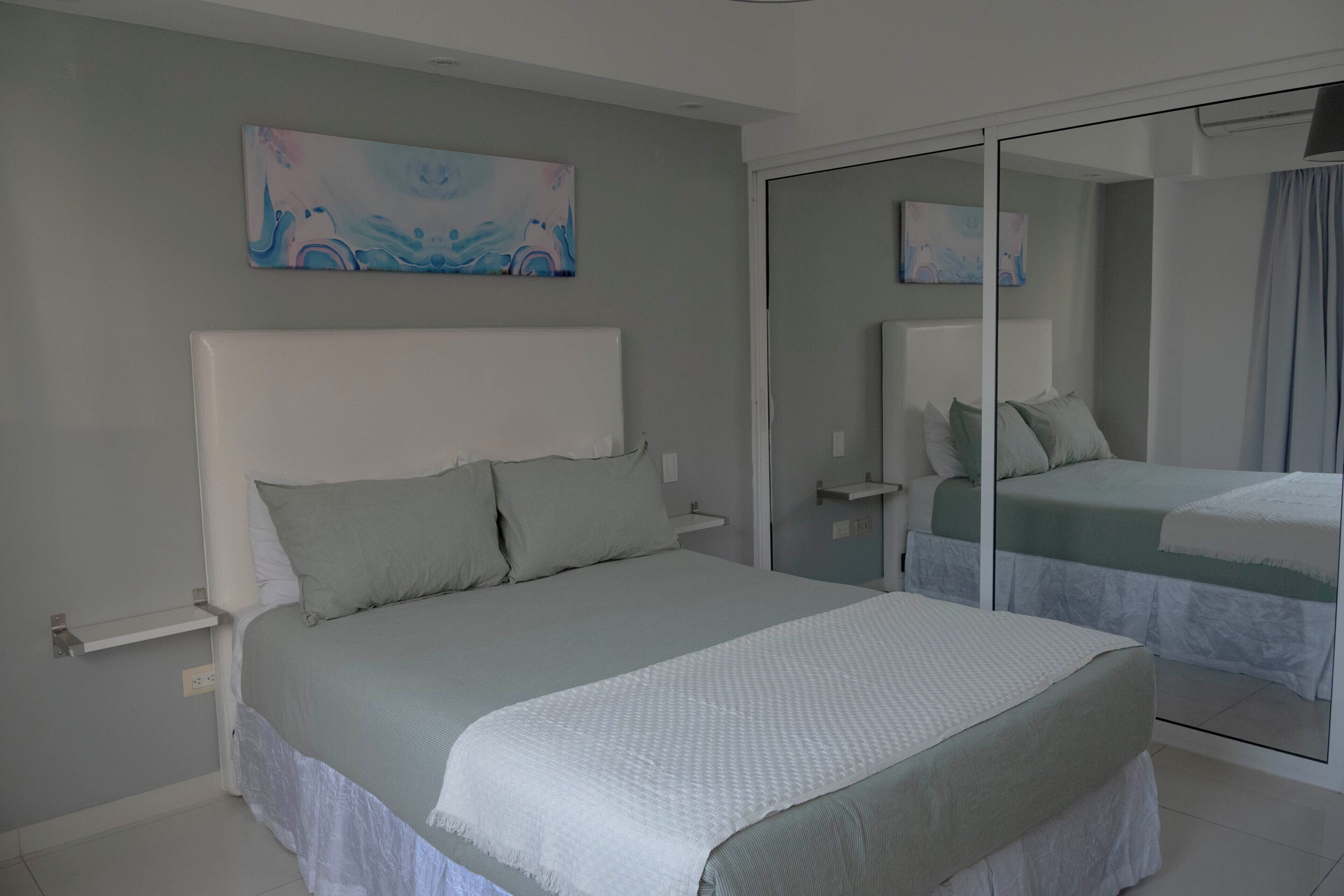 Un dormitorio con una cama grande, una mesita de noche, un espejo y un cuadro en la pared.