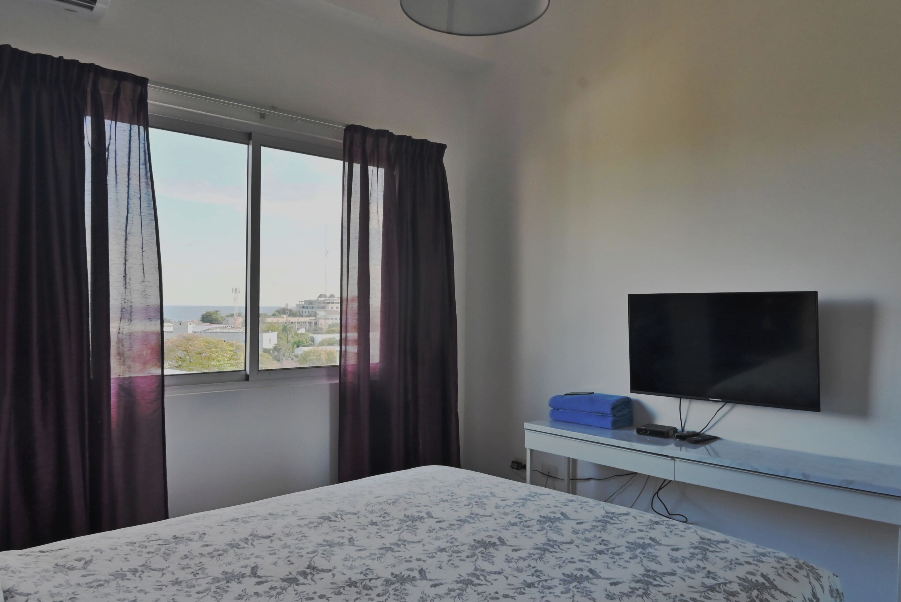 Ein Hotelzimmer mit Bett, Fernseher auf einem Tisch, einem Fenster mit Vorhängen und Blick auf die Stadt.