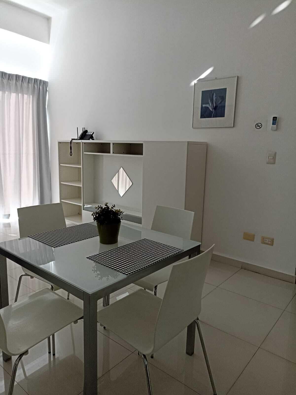 Un comedor moderno y bien iluminado con una mesa de vidrio, sillas blancas y una planta en maceta.