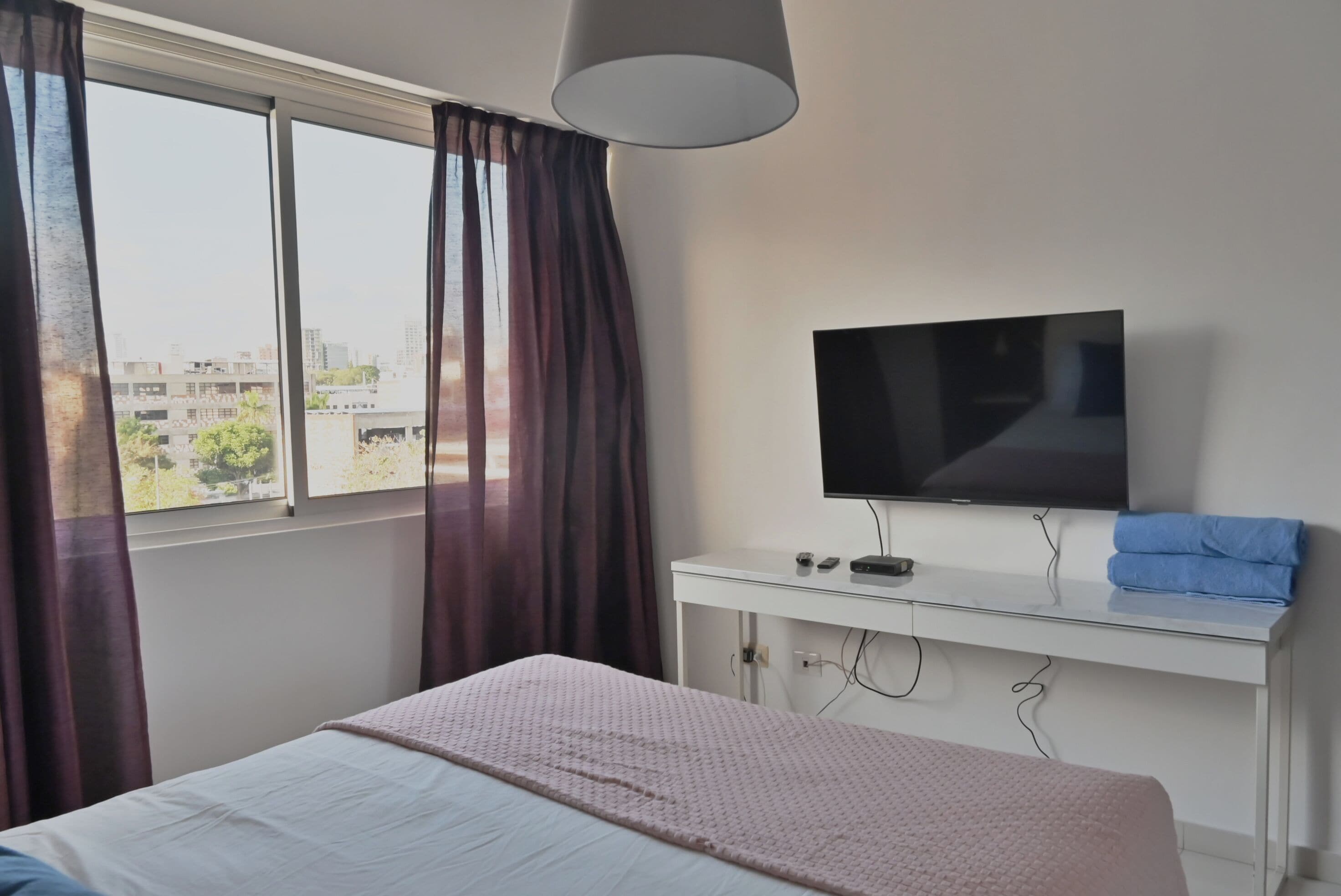 A hotel room with a bed, a TV on a desk, and a window with curtains.