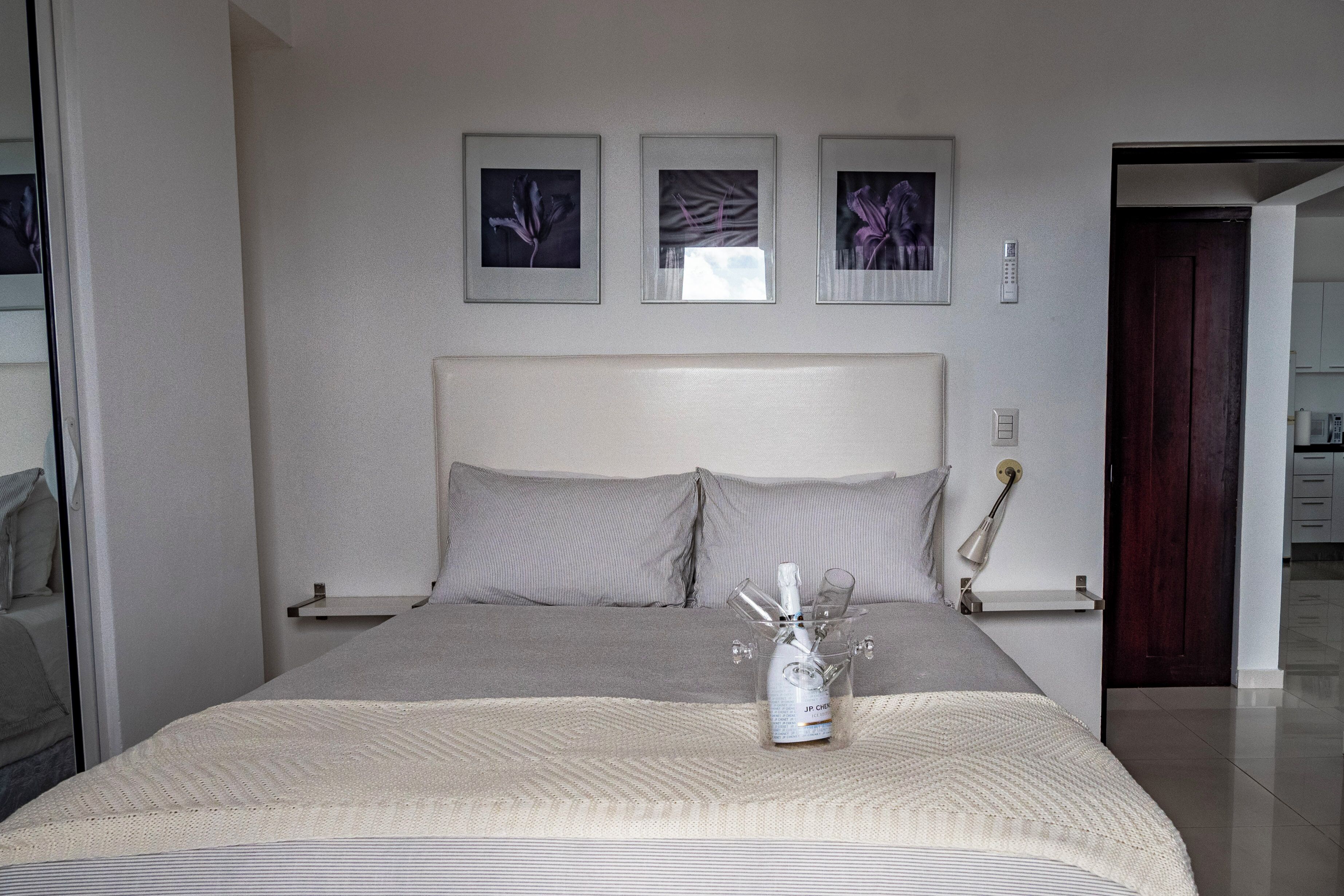 A bedroom with a large bed, a bedside table, and a nightstand. There are three framed pictures on the wall above the bed.