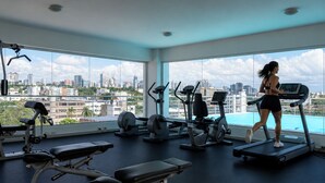 Un gimnasio con cintas de correr, bicicletas estáticas y máquinas de pesas, ventanas amplias con vista a la ciudad.