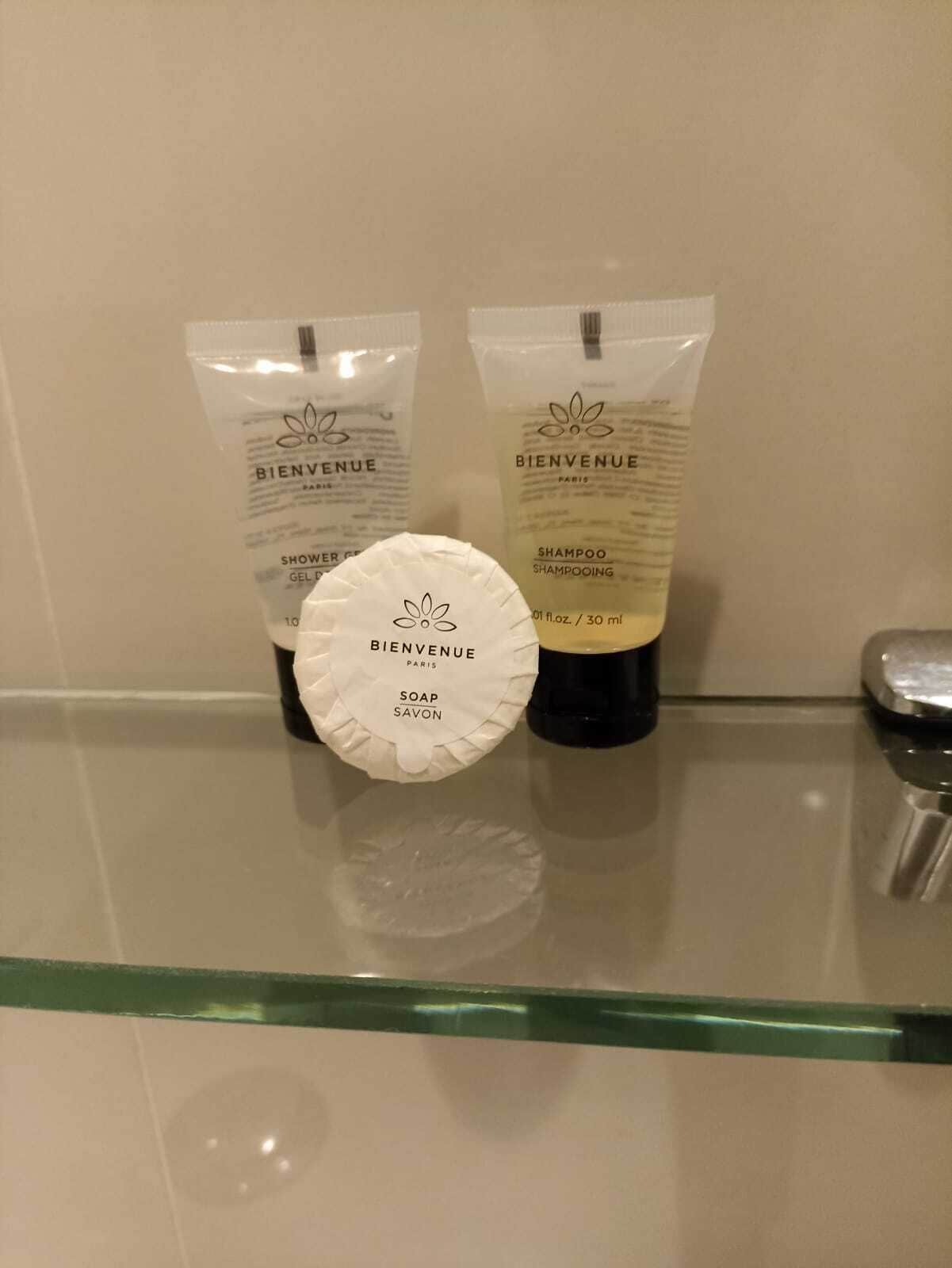 Toiletries on a glass shelf, including a soap bar and two bottles of shampoo.