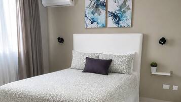 A modern bedroom with a large bed, a ceiling lamp, an air conditioner, abstract wall art, and a small plant.