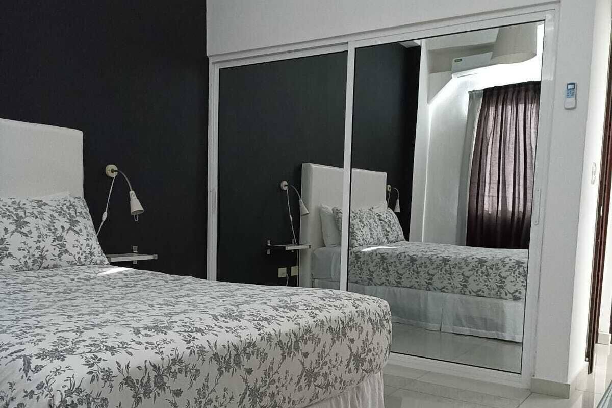 A modern bedroom with a large bed, a nightstand, a lamp, and a sliding glass door leading to a balcony.