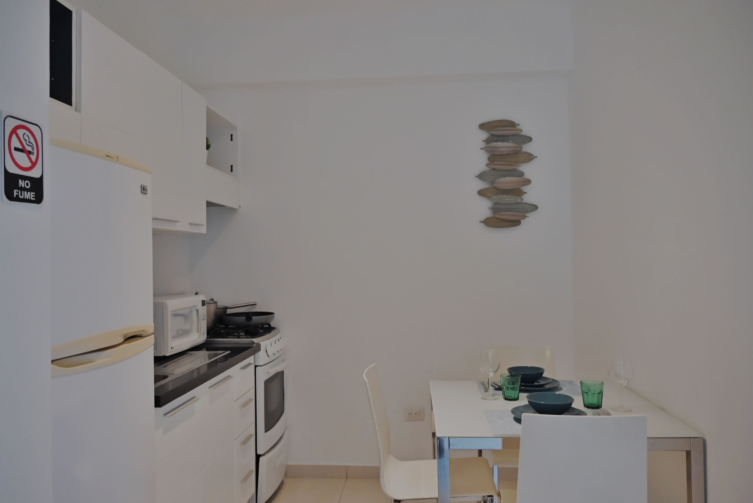 A compact kitchen with a microwave, stove, and cabinets. There's a dining table with a few dishes and glasses.