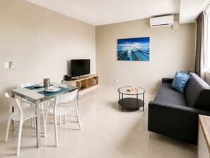A modern living room with a dining area, a flat-screen TV, a painting, and a sofa with cushions. - LINCOLN SUITE (Santo Domingo)