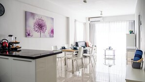 Una cocina moderna con comedor, armarios blancos y un amplio ventanal con cortinas de gasa.