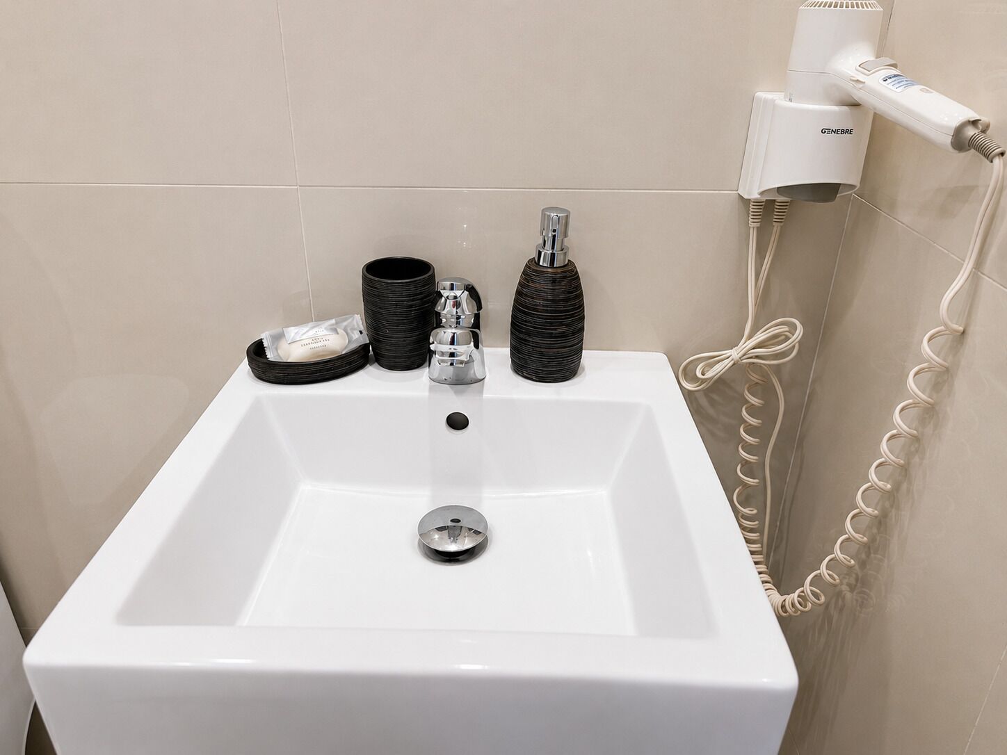 Une salle de bain avec un lavabo blanc, un sèche-cheveux et un téléphone.