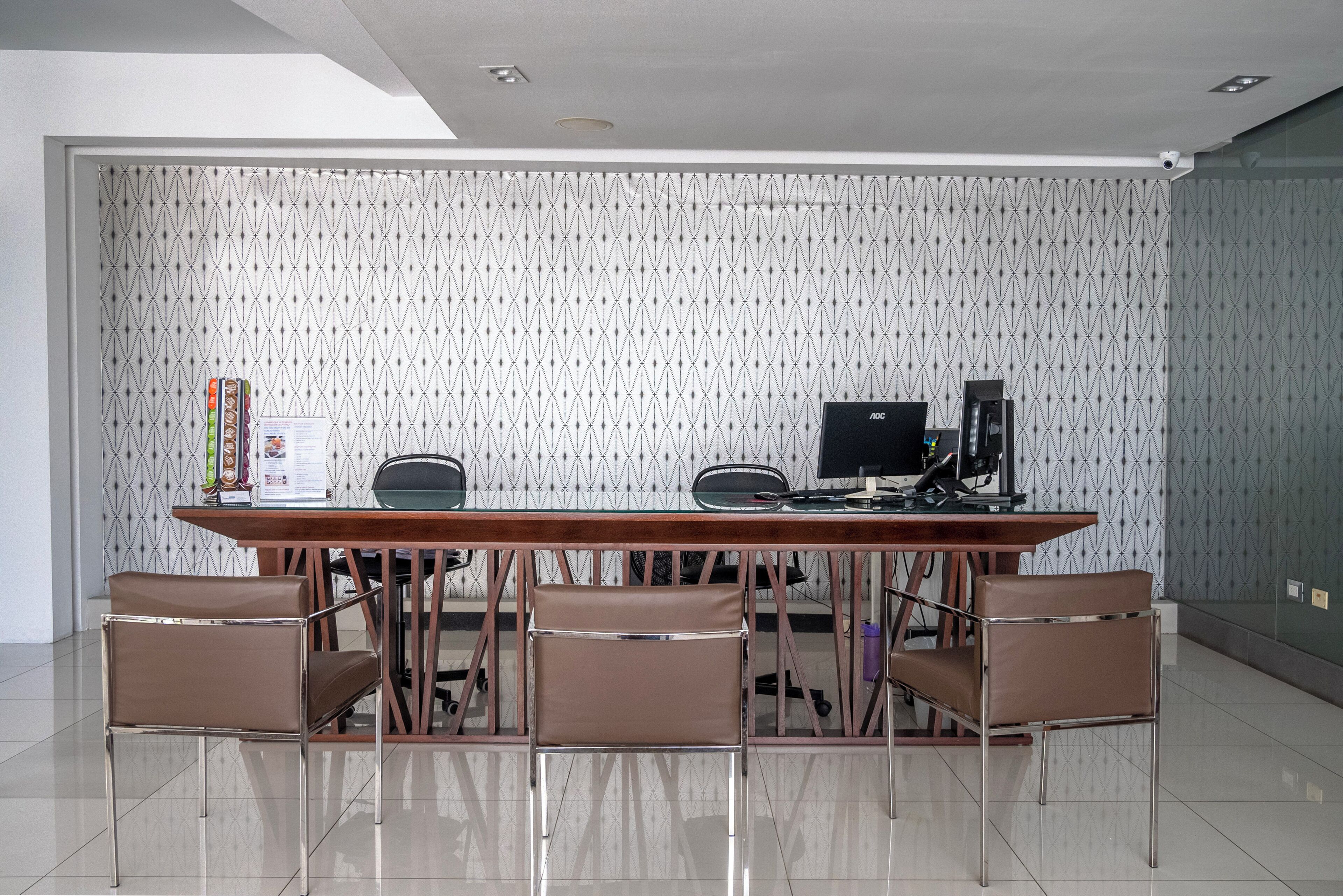 A conference room with a long table, four brown chairs, a computer, and a coffee machine.