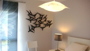 A bedroom with a bed, a chair, a nightstand, a lamp, and a wall art piece. - Apartment La Rochelle Magnifique Vue sur Mer (La Rochelle)