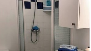 A bathroom with a glass-enclosed shower, white tiles, a sink with a mirror, and a stack of towels. - House in a quiet, sought-after area (Saint-Gilles-Croix-de-Vie)