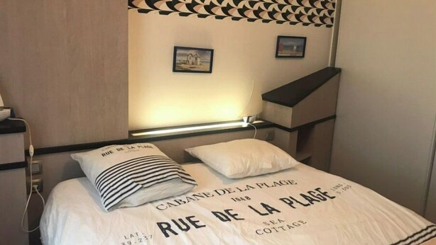 A neatly made bed with a white duvet and pillows, a headboard with a geometric pattern, and a small bedside table with a lamp. - House in a quiet, sought-after area (Saint-Gilles-Croix-de-Vie)