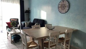A dining area with a wooden table, four chairs, a clock on the wall, and a sofa in the background. - House in a quiet, sought-after area (Saint-Gilles-Croix-de-Vie)