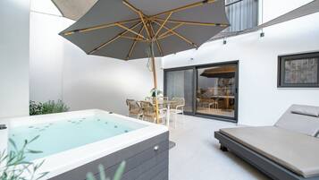 Ein moderner Außenbereich zum Entspannen mit Whirlpool, Liegestuhl und Esstisch mit Stühlen.