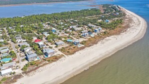Vista aérea de una zona residencial costera con casas a lo largo de la playa, cielos despejados y una gran masa de agua al fondo.