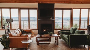 Ein gemütliches Wohnzimmer mit Kamin, großen Fenstern, einer Couch, einem Couchtisch und einem Fernseher.