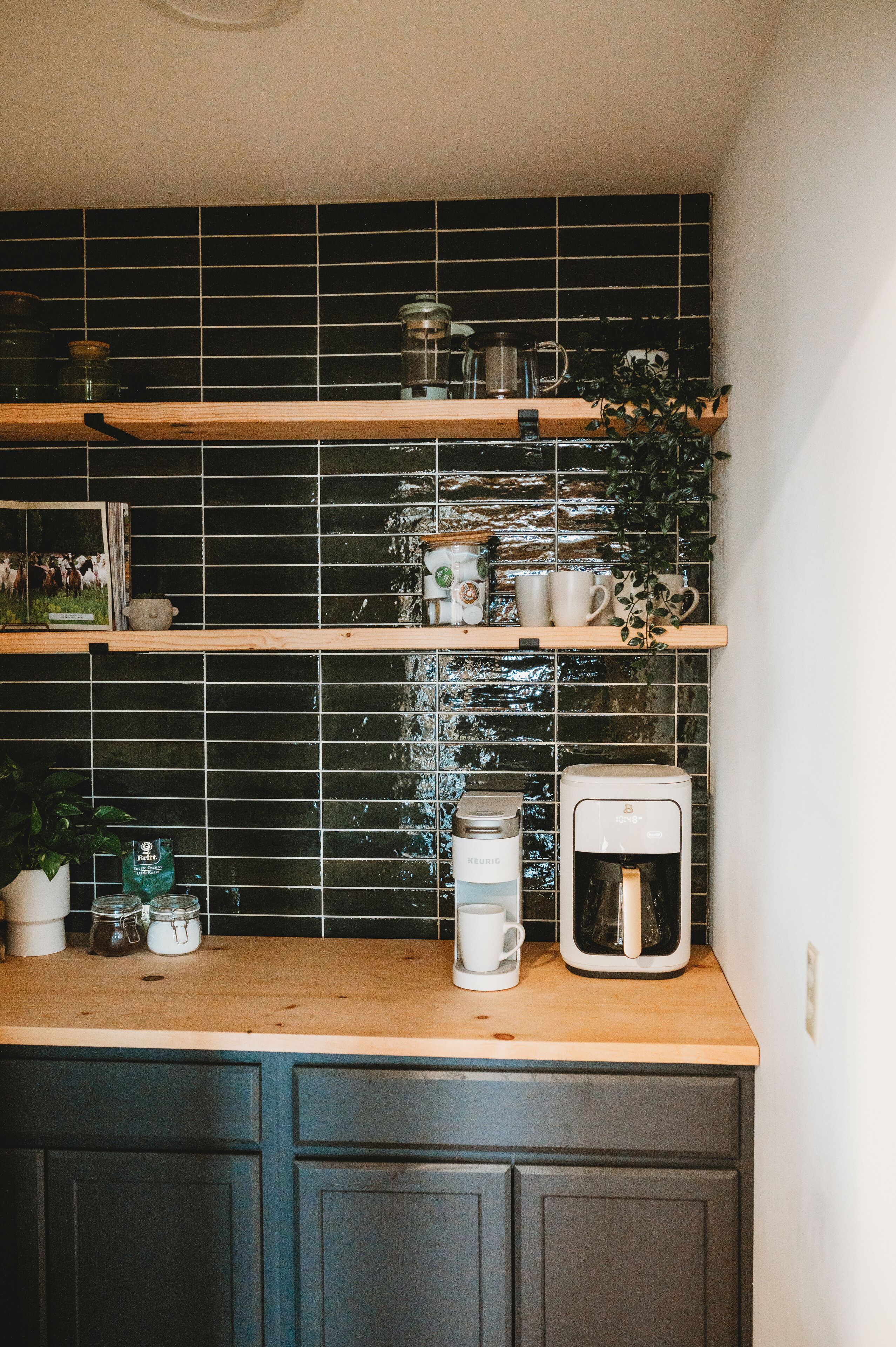 A kitchen with dark tiled backsplash, wooden shelves, and a coffee maker.