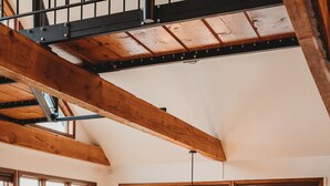 Ein geräumiges Wohnzimmer mit einem grünen Sofa, Holzboden, großen Fenstern und einer hohen Decke mit freiliegenden Balken.
