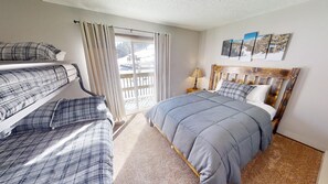 Quarto com beliches, uma cama grande, cabeceira de madeira e uma janela com cortinas.