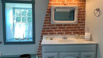 A bathroom with a white vanity, a mirror with a wicker frame, and a window with blue trim.