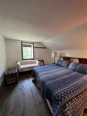 A bedroom with a large bed, a window with blinds, a small table, and a lamp.