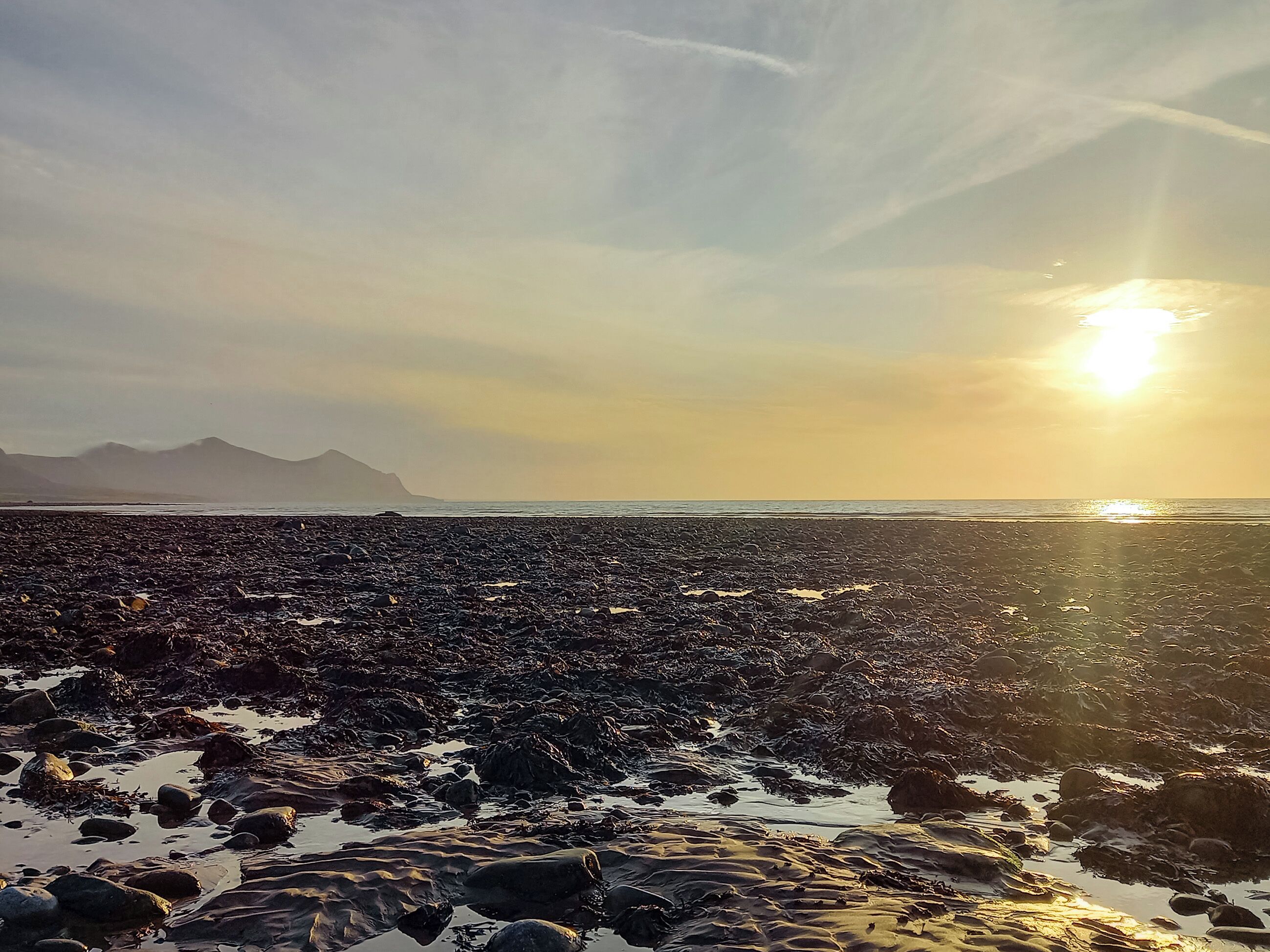 Une plage de galets, avec le soleil couchant à l’horizon.
